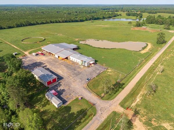 Spacious rural property featuring vast open fields, a pond, and extensive outbuildings for multiple uses.