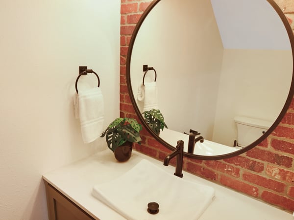 Modern vanity with a round mirror, featuring a brick accent wall and minimalist décor elements.