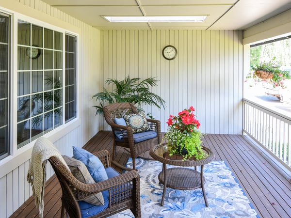Spacious covered porch featuring cozy seating, vibrant plants, and ample natural light for gatherings.