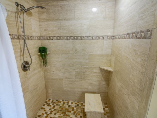 Experience a modern shower space featuring natural stone finishes, a built-in bench, and open design.