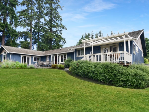 Sprawling blue home with expansive green lawn, surrounded by trees and ideal for outdoor entertaining.