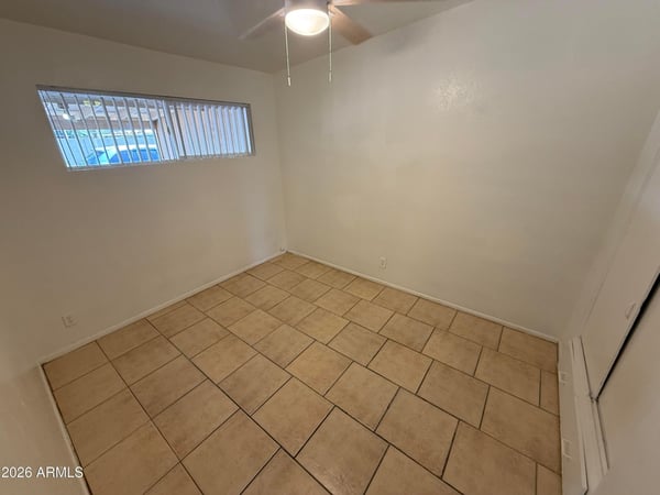 Bright bedroom with tile flooring, ceiling fan, and natural light. The neutral design and comfortable dimensions make it suitable for guests, family members, or a dedicated office space.