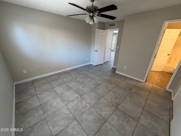 Spacious bedroom featuring tile flooring, ceiling fan, neutral finishes, and convenient access to the bathroom. The flexible layout offers a comfortable and relaxing retreat at the end of the day.