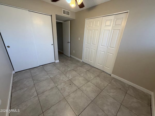 Inviting bedroom with dual closets, tile flooring, ceiling fan, and neutral d cor. Ample storage and a practical layout make this room suitable for guests, family, or a dedicated workspace.