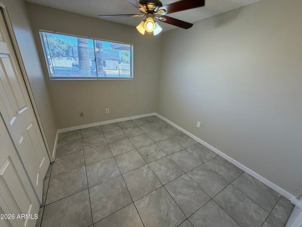 Bright guest bedroom featuring a large picture window, ceiling fan, and low-maintenance tile flooring. Natural light and neutral finishes create a welcoming atmosphere throughout the space.