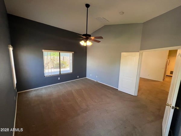 Large primary suite offering soaring ceilings, plush carpeting, and ample space for a full bedroom set. Multiple windows provide natural light and enhance the welcoming atmosphere.