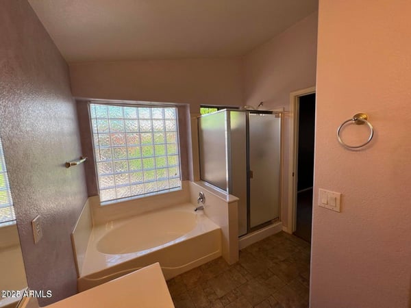 Primary bathroom designed for relaxation with a garden tub, separate shower, tile flooring, and large window. The bright and functional layout adds comfort and value to this Goodyear home.