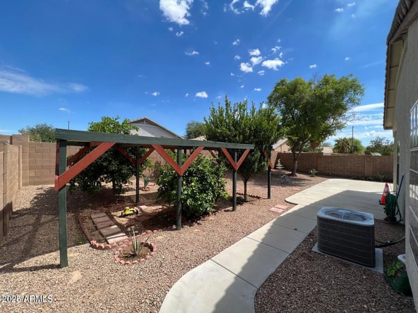 Spacious backyard with mature trees, low-maintenance desert landscaping, and a charming shaded garden structure. An inviting outdoor setting with room to enjoy and personalize.