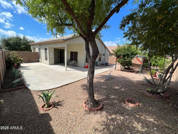 Inviting backyard with mature trees, desert landscaping, and a spacious covered patio. The thoughtfully designed outdoor space provides shade, privacy, and plenty of room for gatherings, recreation, or peaceful relaxation.