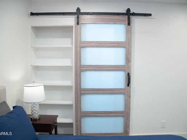 A contemporary sliding barn door and built-in shelving create both style and functionality within the primary bedroom. These custom touches enhance the remodeled interior and modern aesthetic throughout the home.