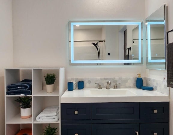 This updated bathroom showcases a sleek vanity, generous storage, illuminated mirrors, and modern finishes. The thoughtful remodel delivers both convenience and contemporary design.