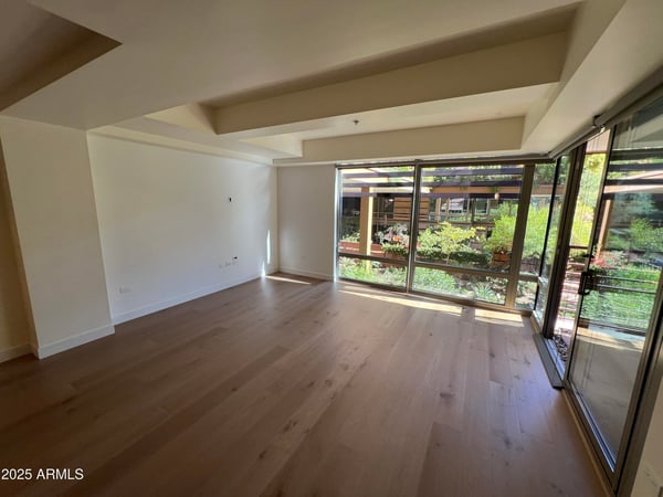 Bright living room with expansive windows overlooking beautifully landscaped community grounds. Wood flooring and an open layout enhance the home's contemporary appeal.