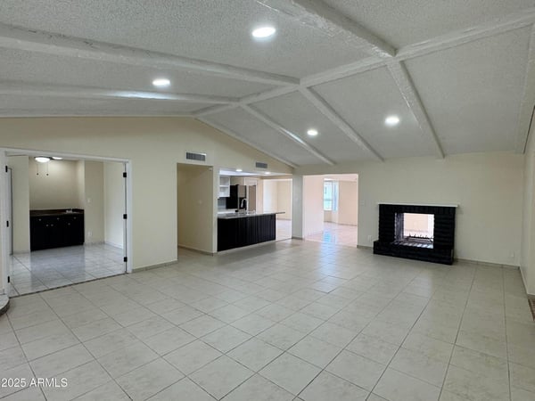 Open living room with dramatic wood-beamed ceilings, tile flooring, and a statement fireplace. The spacious design offers flexibility for entertaining and comfortable daily living.