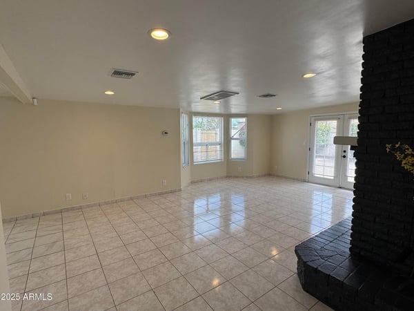 Inviting family room centered around a dramatic fireplace with abundant natural light and backyard access through French doors. The spacious layout offers flexibility for relaxation, entertaining, and indoor-outdoor living.