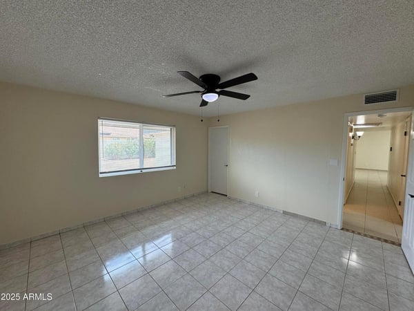 Comfortable guest bedroom featuring neutral finishes, tile flooring, and a ceiling fan. Large windows provide natural light while maintaining a clean, move-in-ready appearance.