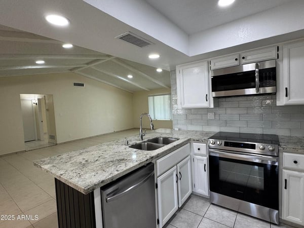 Contemporary kitchen showcasing granite counters, stainless steel appliances, abundant cabinetry, and a large peninsula overlooking the living room. The open layout creates a seamless connection between cooking, dining, and gathering spaces.