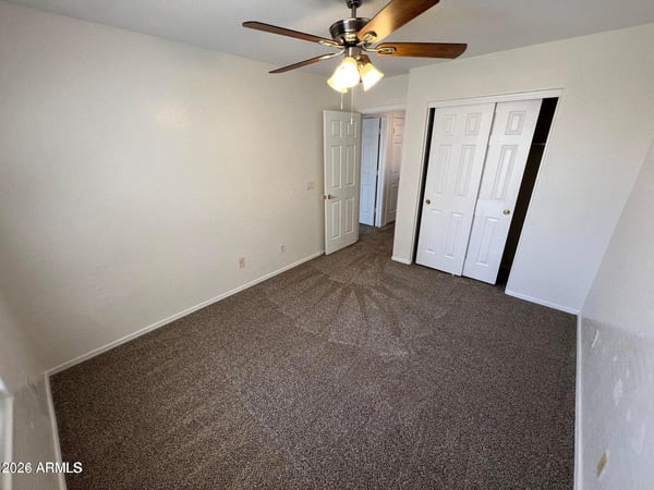 Bright guest bedroom showcasing fresh carpeting, neutral finishes, ceiling fan, and ample closet space. The functional layout makes this room ideal for visitors, family members, or a dedicated workspace.