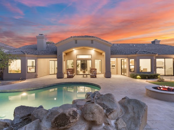 Resort-inspired backyard featuring a sparkling swimming pool, fire pit, natural rock accents, expansive patio, and covered outdoor living area. A perfect Scottsdale retreat for entertaining, relaxing, and enjoying Arizona's year-round sunshine.