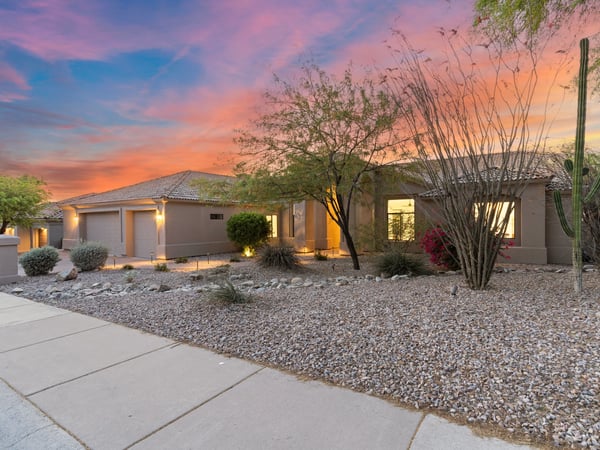 Inviting front exterior showcasing mature desert landscaping, modern architecture, and a spacious three-car garage. The professionally designed landscape enhances the home's impressive curb appeal and low-maintenance lifestyle.