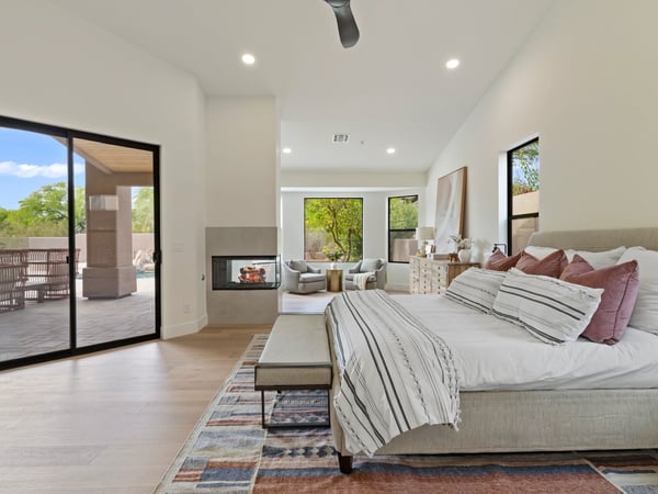 Beautiful primary bedroom featuring a fireplace, comfortable sitting area, large sliding glass doors, and peaceful backyard views. This luxurious Scottsdale retreat offers a relaxing atmosphere with elegant finishes and direct access to the outdoor living spaces.