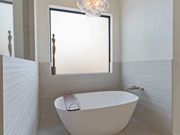 Elegant soaking tub surrounded by designer tile, oversized window, and modern lighting. A peaceful retreat designed for comfort and relaxation within the luxurious primary suite.