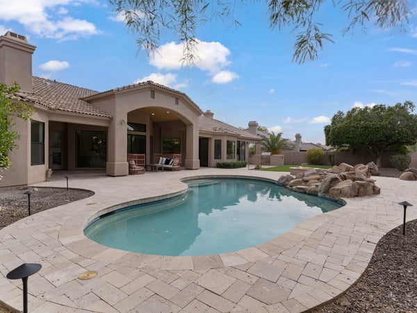 Beautiful outdoor living space featuring a sparkling swimming pool, expansive paver patio, artificial turf, mature landscaping, and generous entertaining areas in this Scottsdale home.