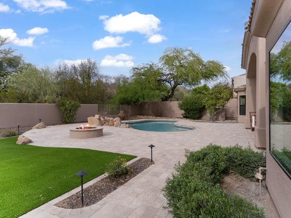 Private Scottsdale backyard featuring a sparkling swimming pool, custom fire pit, expansive paver patio, artificial turf, and mature landscaping designed for relaxing and entertaining.