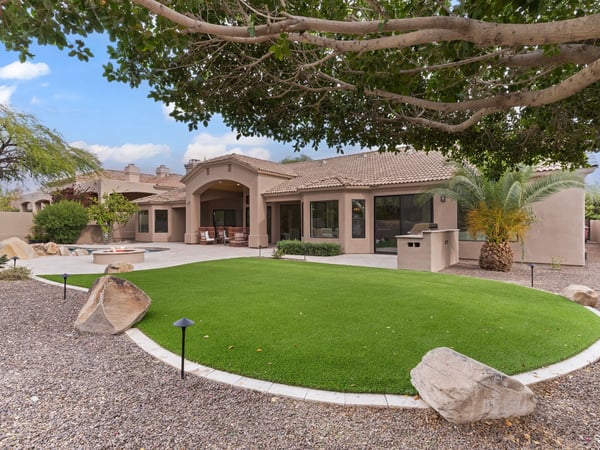 Resort-inspired backyard with a covered patio, sparkling pool, outdoor kitchen, artificial lawn, and generous entertaining space. A beautiful extension of this Scottsdale home's luxury living.