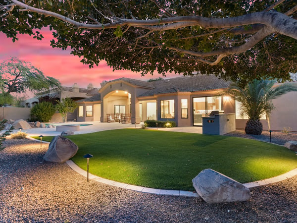 Beautiful evening exterior highlighting the pool, covered patio, outdoor seating, lush landscaping, and custom BBQ area. This Scottsdale property is ideal for entertaining day or night.