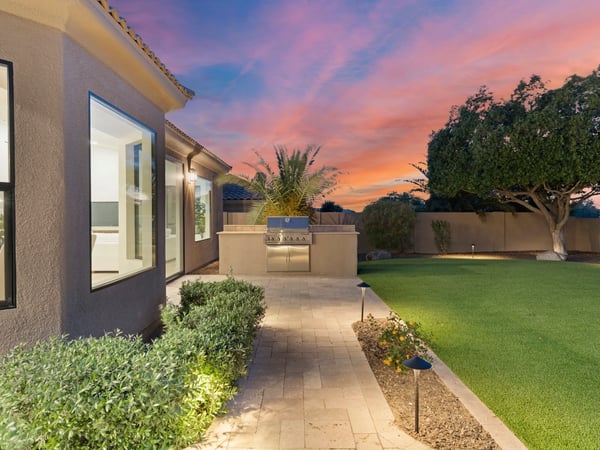 Custom outdoor kitchen with built-in grill surrounded by elegant paver walkways, artificial turf, and landscape lighting. A perfect Scottsdale backyard for hosting family and friends.