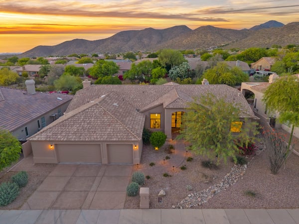 Twilight aerial showcasing the welcoming front elevation, spacious three-car garage, and professionally landscaped front yard. Located in a sought-after Scottsdale neighborhood with scenic mountain views.