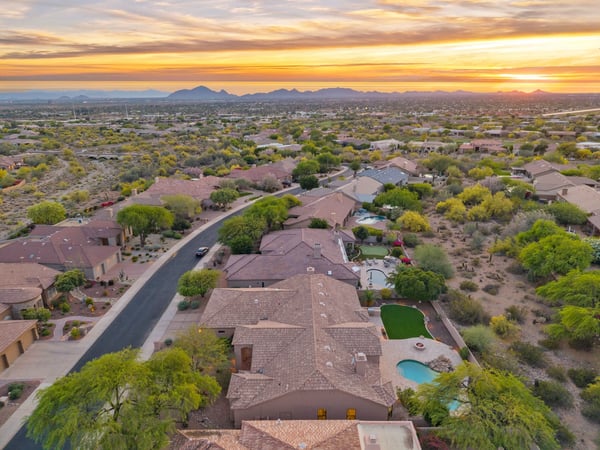Expansive aerial capturing the surrounding Scottsdale neighborhood, dramatic mountain scenery, nearby desert wash, and the home's desirable location among beautifully maintained luxury residences.