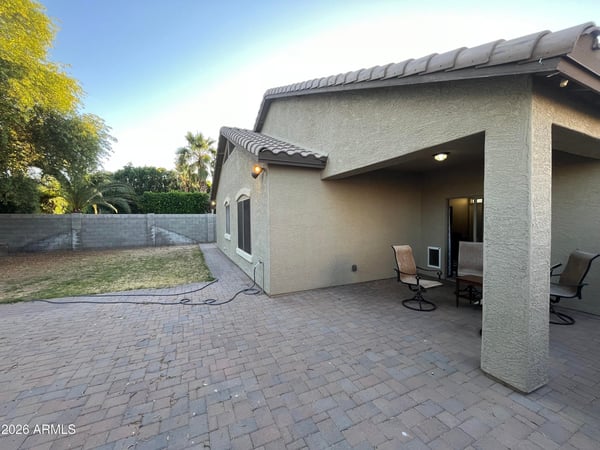 Backyard view featuring an extended paver patio, covered seating area, and lawn space that offers flexibility for outdoor entertaining and everyday enjoyment.
