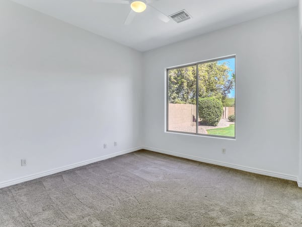 Large windows fill this spacious bedroom with natural light while providing views of the landscaped backyard. Plush carpeting and high ceilings create a comfortable retreat within this Glendale home.
