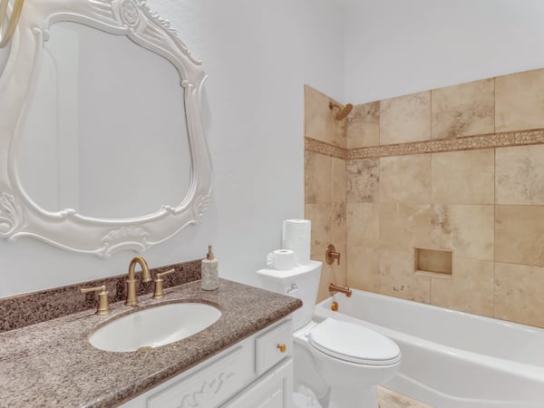 Featuring a granite vanity, elegant fixtures, decorative framed mirror, and tiled tub and shower surround, this full bathroom blends functionality with timeless design in this Glendale property.