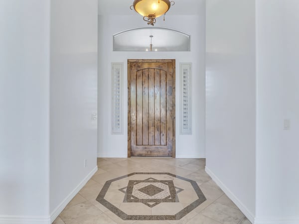 The inviting foyer features a custom wood entry door, decorative tile inlay, soaring ceilings, plantation shutters, and timeless architectural details that create a memorable welcome in this Glendale residence.