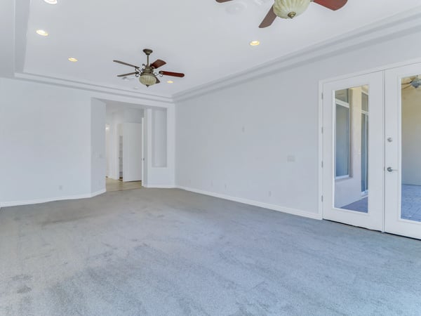 Elegant primary bedroom featuring French doors to the covered patio, tray ceiling, dual ceiling fans, plush carpeting, and abundant natural light. This Glendale home offers a relaxing private retreat.