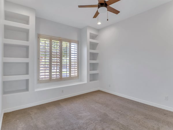 This inviting bedroom features plantation shutters, built-in shelving, plush carpeting, soaring ceilings, and abundant natural light. A flexible living space ideal for guests, family, or a private office in Glendale.