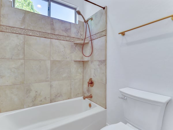 This full bathroom features a tiled tub and shower combination with decorative accents, updated fixtures, and natural lighting from a large window. A stylish and practical addition to this Glendale property.
