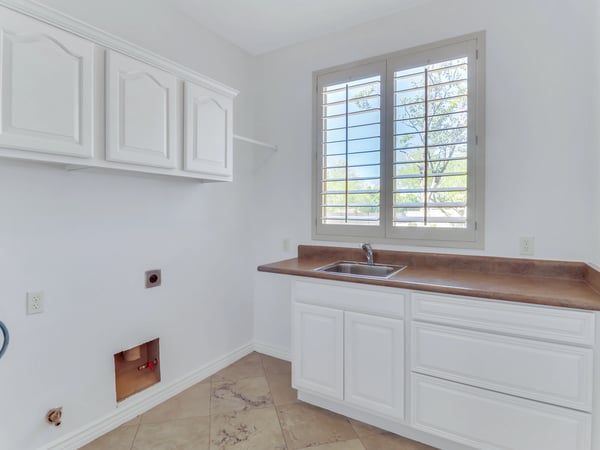 Well-equipped laundry room featuring built-in cabinetry, utility sink, countertop workspace, plantation shutters, and durable tile flooring. This Glendale residence provides excellent organization and everyday functionality.