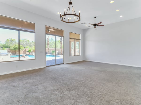Spacious living room filled with natural light through oversized windows and sliding glass doors that frame beautiful backyard views. The open design enhances comfort while creating effortless indoor-outdoor living.