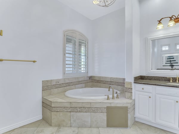 The primary bathroom features a spacious soaking tub with tiled surround, granite vanity, plantation shutters, and elegant finishes, providing a relaxing spa-inspired experience in this Glendale home.
