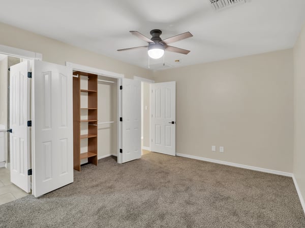 Bright guest bedroom with neutral carpeting, ceiling fan, generous closet storage, and built-in shelving. This flexible living space adds comfort and functionality to this updated Phoenix rental.