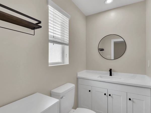 Modern bathroom featuring a quartz vanity, contemporary cabinetry, matte black faucet, and stylish round mirror. Updated finishes create a clean, inviting space in this Phoenix rental.