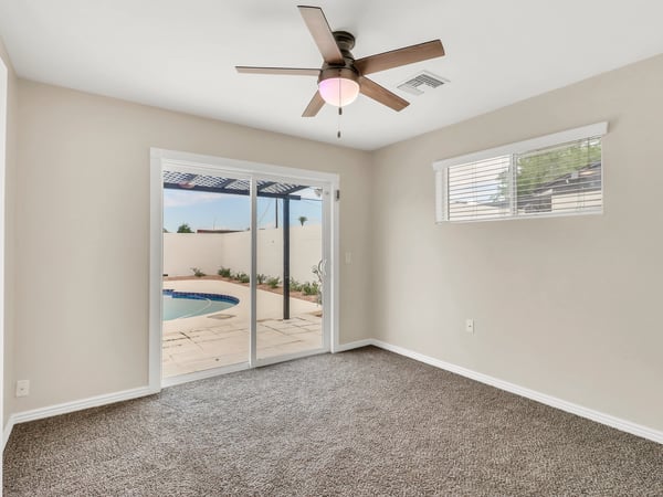 Spacious bedroom with sliding glass doors leading directly to the backyard and pool area, plush carpeting, and a ceiling fan. Enjoy private indoor-outdoor living in this remodeled Phoenix rental.