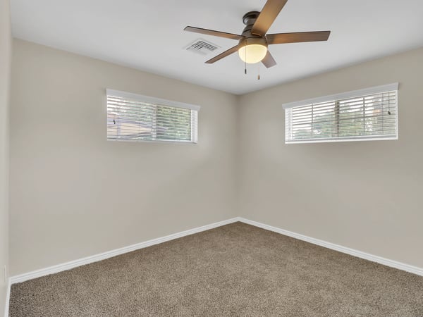 Bright bedroom offering plush carpeting, ceiling fan, dual windows, and neutral colors ready to fit your lifestyle. A versatile room in this move-in-ready Phoenix rental.