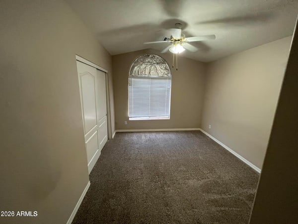 Featuring soft carpeting, a ceiling fan, an arched window, and ample closet space, this inviting bedroom offers flexibility for guests, family, or a home office.