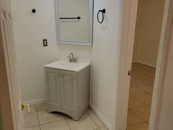 Bright bathroom featuring a modern vanity and ample tile space, leading into an additional room beyond.