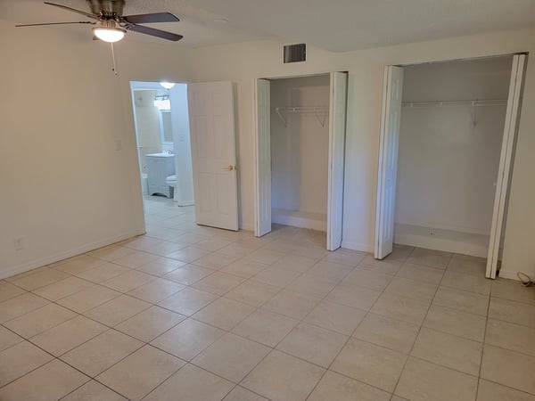 Spacious bedroom featuring tile flooring, dual closets, and an adjoining bath for convenient living.