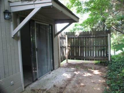 Private outdoor space featuring a sliding door entrance, surrounded by foliage and a wooden fence.
